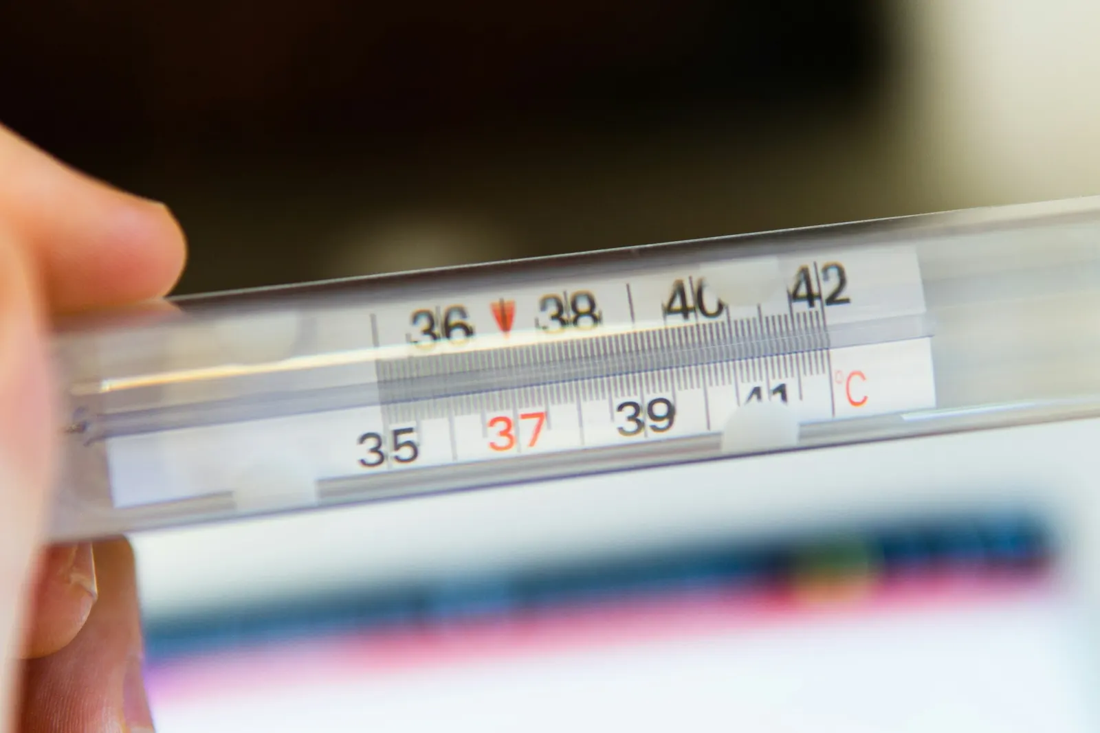 A glass thermometer held in a hand, with its scale marked from 35 to 42 degrees